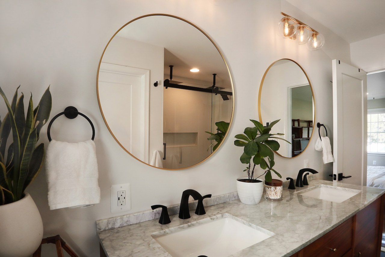 elegant bathroom remodel featuring double vanity with marble countertop and round mirrors